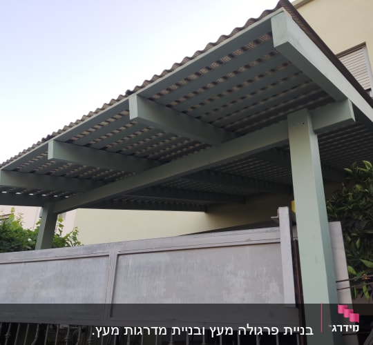פרגולה מעץ עם גג מתכת ליד גדר